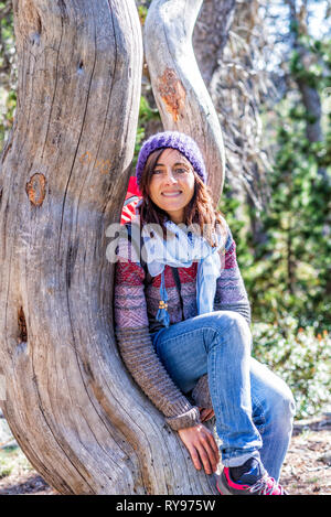 Retrato de mujer sonriente caminante sentado en el árbol en el bosque