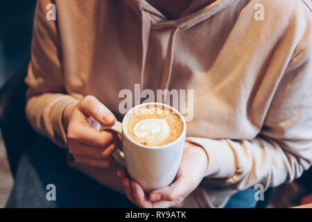 Taza de café capuchino con espuma de corazón en manos femeninas en el cafe, cerrar