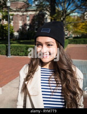 Hermosa joven está cerca de los edificios de la Universidad de Columbia en Nueva York, Estados Unidos. Elegante kazajo sonriente estudiantil femenina en el fondo del campus. Foto de stock