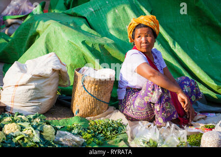 Una mujer sentada sobre una lona verde vendiendo verduras en Kalaw mercado, Myanmar