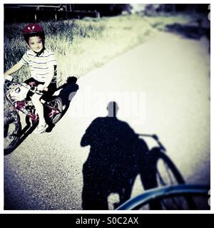 Un niño de siete años monta su bicicleta pasando por un hombre en una bicicleta de ruta. Foto de stock