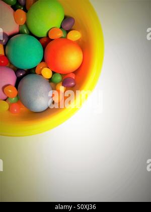 Huevos coloridos y jelly beans en un tazón visto desde arriba sobre fondo blanco.