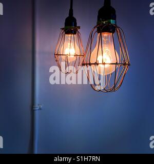 Dos luces de tungsteno cuelgue delante de una pared vacía con un sólo conducto eléctrico sobre ella Foto de stock