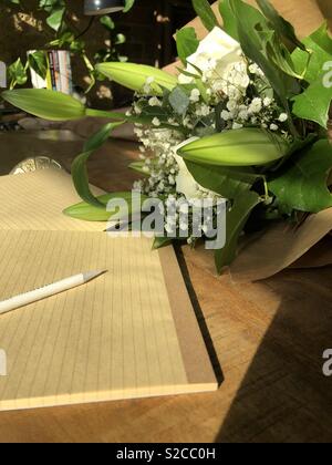Portátiles en un escritorio de madera con un ramo de flores crema envuelto en papel marrón Foto de stock