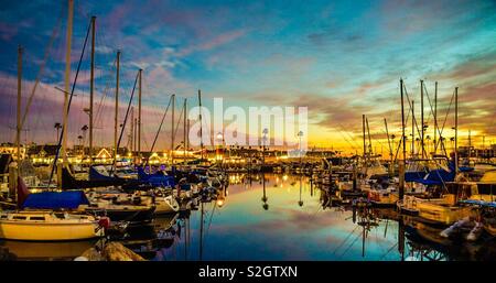 Sunset Harbour, filas de barcos, palmeras y un faro contra un colorido atardecer. Todo se refleja en el agua. Foto de stock