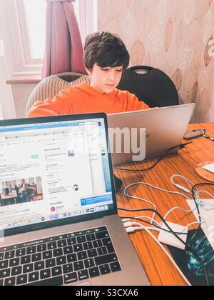 Un joven niño en la escuela en casa durante el cierre de Covid en el Reino Unido con el portátil de sus padres en primer plano. Foto de stock