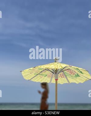 Selecciona el enfoque en un paraguas colorido en miniatura con una mujer borrosa y. fondo de agua del océano Foto de stock