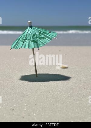 Selecciona el enfoque en una sombrilla verde en miniatura con fondo de playa borroso Foto de stock