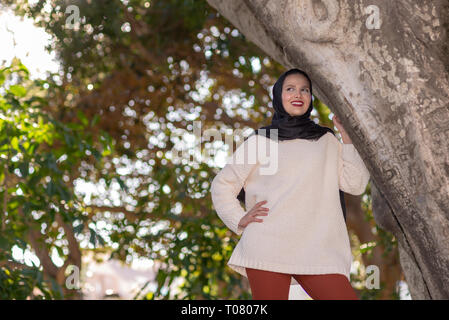 Hermosa mujer musulmana en ropa formal y hijab haciendo compras en línea  con tarjeta de crédito y smartphone. Señorita de pie cerca del edificio de  oficinas y disfrutando de un pago fácil