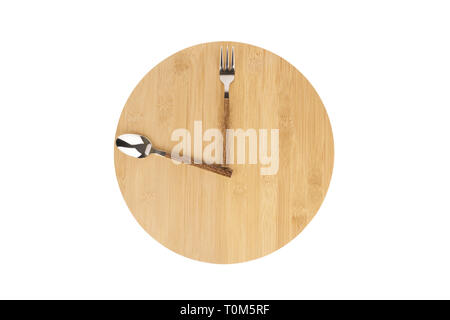 Tenedor y cuchara dispuestas en una placa de madera redondo para indicar la hora de almuerzo como un reloj. Foto de stock