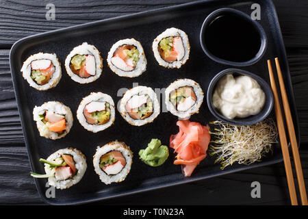 Conjunto de rodillos Uramaki servidos con salsas, brotes de soja, jengibre y wasabi closeup en una placa en la tabla superior horizontal vista desde arriba Foto de stock