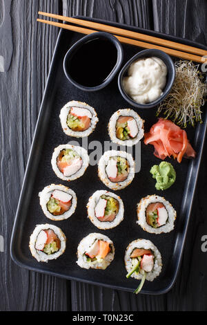 Conjunto de rodillos Uramaki servidos con salsas, brotes de soja, jengibre y wasabi closeup sobre un plato en la mesa. Vista superior de la vertical desde arriba Foto de stock