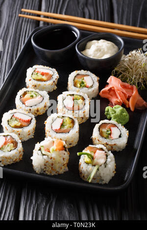 Rollos de sushi Uramaki servidos con salsas, jengibre y wasabi closeup en una placa en la tabla vertical. Foto de stock