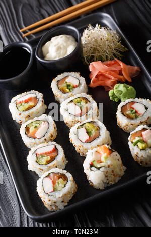 Conjunto de rodillos japonesa uramaki servidos con salsas, jengibre y wasabi closeup en una placa en la tabla vertical. Foto de stock