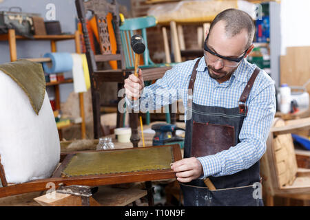 Obrero calificado en silla de tapicería de muebles taller de reparación Foto de stock