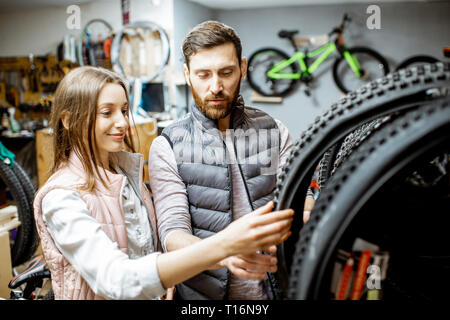 Vendedor joven ayudando a elegir un nuevo neumático de la bicicleta en la tienda de deportes Foto de stock