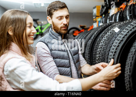 Vendedor joven ayudando a elegir un nuevo neumático de la bicicleta en la tienda de deportes Foto de stock