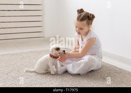 La gente, los niños y las mascotas concepto - niña chica sentada en el piso con el lindo perrito Jack Russell Terrier y jugando