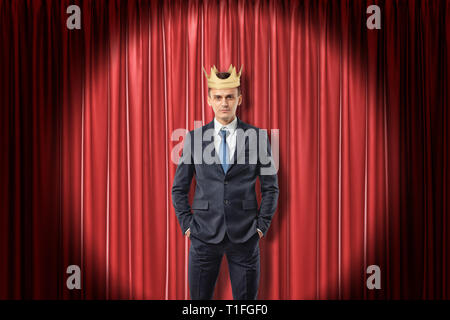 Joven empresario vistiendo la corona de oro sobre fondo rojo telones Foto de stock
