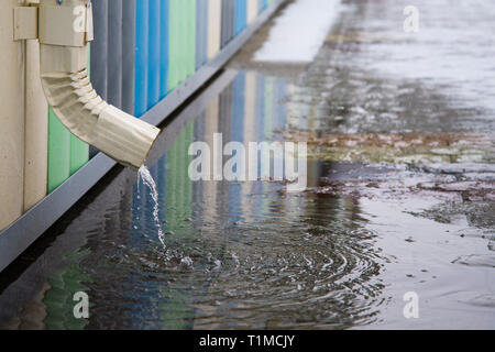 Desagüe blanco con pavimento inundadas. El agua de lluvia que fluye desde el tubo de desagüe closeup.