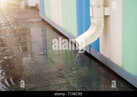 Desagüe blanco con pavimento inundadas. El agua de lluvia que fluye desde el tubo de desagüe closeup.