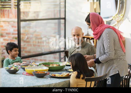 Madre en el hijab sirviendo la cena con la familia en la mesa de comedor Foto de stock