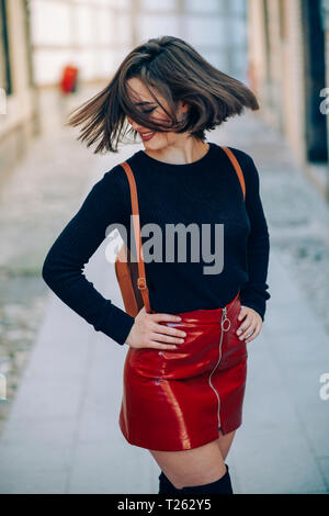 Sonriente joven mujer vistiendo falda de charol roja con cremallera tirando su cabello Fotografía de stock Alamy