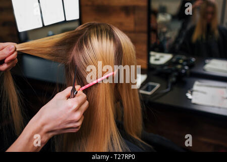Peluquero manos sosteniendo hebra de cabello rubio mientras realizas antes de corte de pelo en el salón Foto de stock