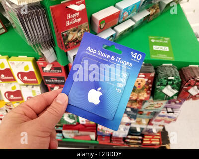 PLATTSBURGH, USA - Enero 21, 2019 : Apple Itunes tarjeta de regalo de 40 dólares en una mano encima de una estantería con diferentes tarjetas de regalos en una tienda de Walmart. Foto de stock