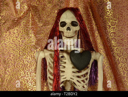 Anti-Valentine esqueleto con negro quemado de carbón y corazón rojo y púrpura brillante pelo contra el oro en forma de remolino y cortinas rojas Foto de stock