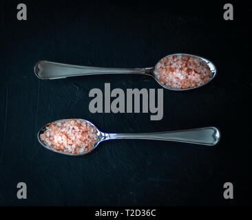 La sal cristalina del Himalaya rosada en cucharas sobre un fondo de placa negra Foto de stock