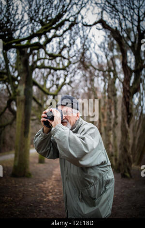 Hombre Senior dedicar tiempo a su pasatiempo favorito - Fotografía - tomando fotos con su cámara digital exterior/DSLR Foto de stock