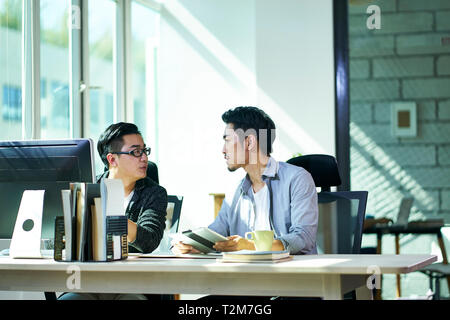 Dos jóvenes ejecutivos asiáticos trabajan juntos hablando de plan de negocios en la oficina. Foto de stock