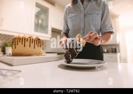 Cerca de chef femenina colocando un trozo de pastel en la placa con la cuchilla. El chef prepara un delicioso postre.