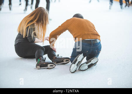 Mujer caen hacia abajo mientras que el patinaje. hombre ayudando a sus actividades deportivas. Foto de stock