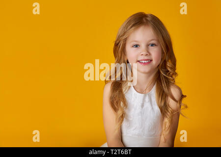 Retrato de una linda niña de 6 años con un vestido blanco posando sobre un  amarillo brillante