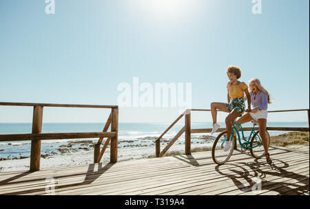 Las mujeres jóvenes alegres bicicleta juntos. Mejores amigos divirtiéndose en una bicicleta en la rambla costera. Foto de stock