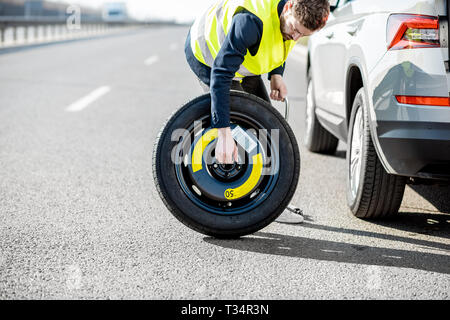 El hombre cambiando la rueda con rueda de repuesto permanente cerca del coche rotos en la carretera