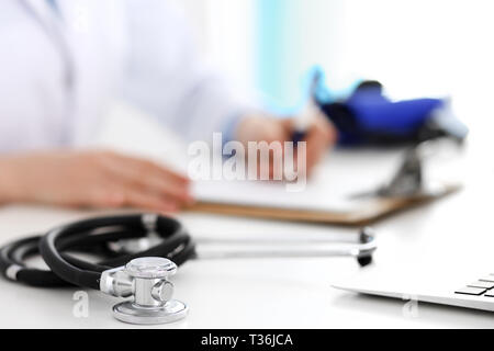 Primer plano de un estetoscopio. Doctora llena formulario médico mientras está sentado en el escritorio en el hospital. Salud, Trabajo y medicina en cardiología Foto de stock