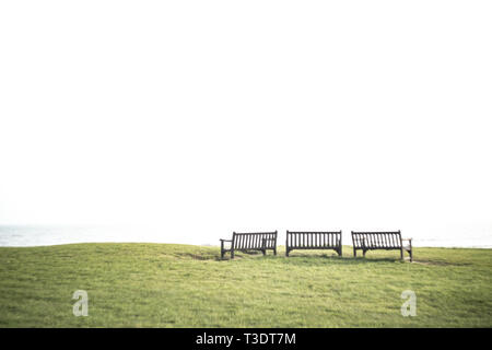 Tres bancos en la hierba con el espacio en blanco que habrá por encima (Copiar área vacía), podría simbolizar la soledad, el vacío, la depresión, la tranquilidad, la evasión. Foto de stock