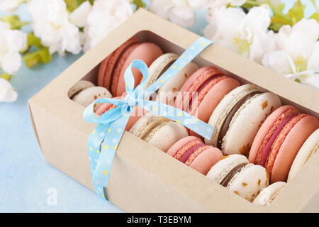 Pink macarons en una caja decorada con cinta y flores sobre fondo azul. Postre francés. Foto de stock