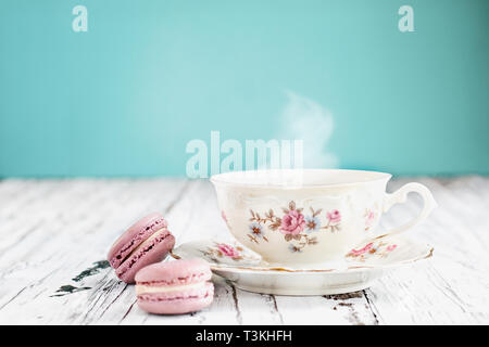 Antique Baviera Winterling footed taza de té desde los 1950s' con pink macarons en una rústica mesa blanca contra un fondo de color verde azulado. Foto de stock