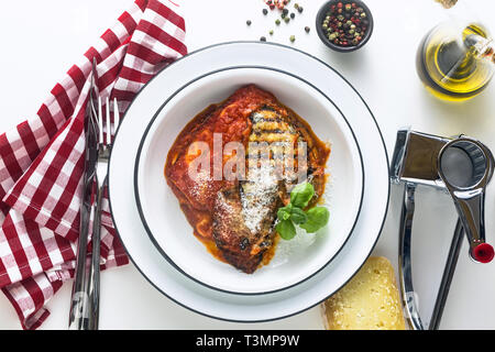 Melanzane alla parmesana plato italiano, hecho de berenjenas y los tomates en una tabla, servido en un plato con queso y albahaca cocina tradicional. Foto de stock