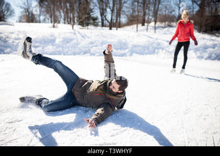 Hombre caucásico cayendo mientras que el patinaje sobre hielo en el lago congelado Foto de stock