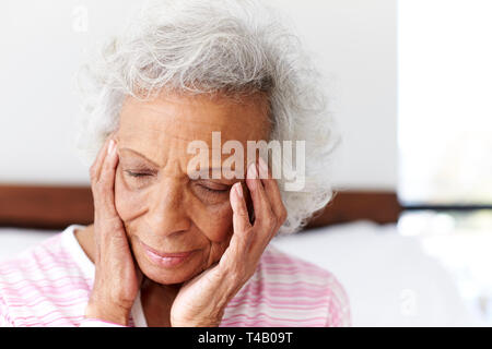 Mujer mirando deprimido infeliz sentado en el lado de la cama, en su casa con la cabeza entre las manos