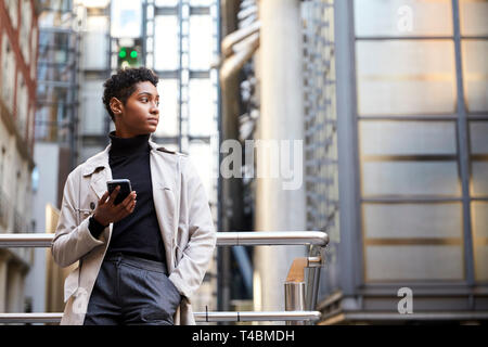 Moda joven negra de pie en la ciudad la celebración de smartphone, ángulo bajo