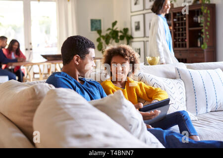 Padre pasar tiempo con su hija pre-adolescentes en un sofá en el salón, madre caminando por la habitación, y los abuelos sentados en una mesa al fondo