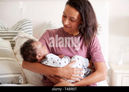 Los jóvenes adultos de raza mixta madre sentada en su cama y sostiene a su hijo en sus brazos, cintura, cierre arriba