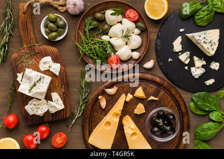 Variedad de quesos, aceitunas y hierbas frescas sobre fondo de madera, vista superior. Foto de stock