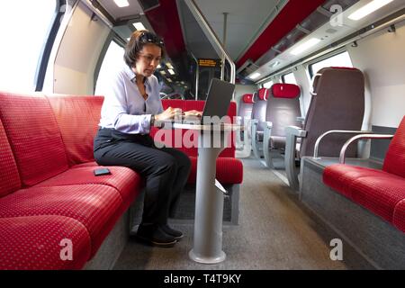 Mujer de negocios sentada en el tren de primera clase, trabajando con un ordenador portátil y un teléfono móvil, Suiza